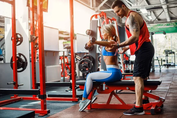 Sporty girl doing weight exercises with assistance of her personal trainer at gym. — Stock Photo, Image