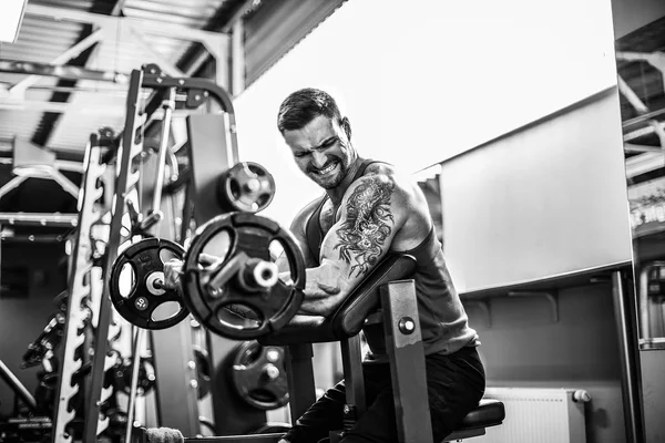 Hombre culturista haciendo el conjunto de un ejercicio de barra en un gimnasio . — Foto de Stock