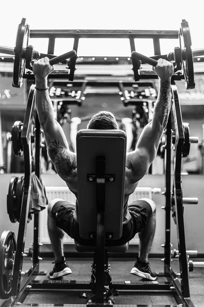 Homem fazendo um exercício para os ombros no simulador — Fotografia de Stock