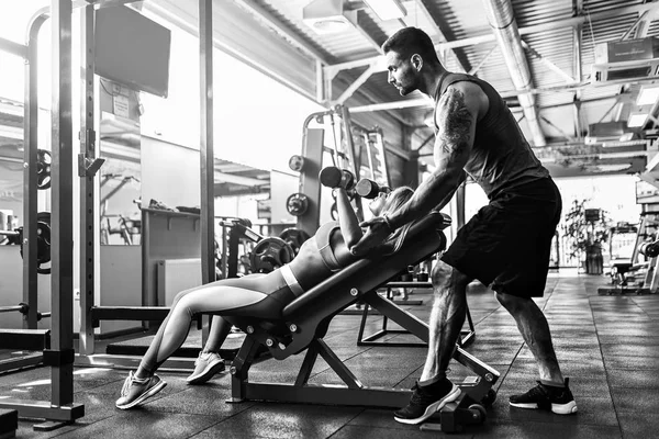 Ragazza sportiva che fa esercizi di peso con l'assistenza del suo personal trainer in palestra . — Foto Stock