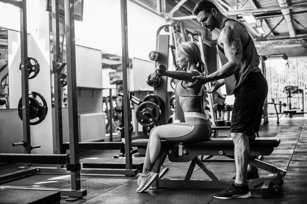 Sportieve meisje doet gewicht oefeningen met hulp van haar persoonlijke trainer bij gym. — Stockfoto