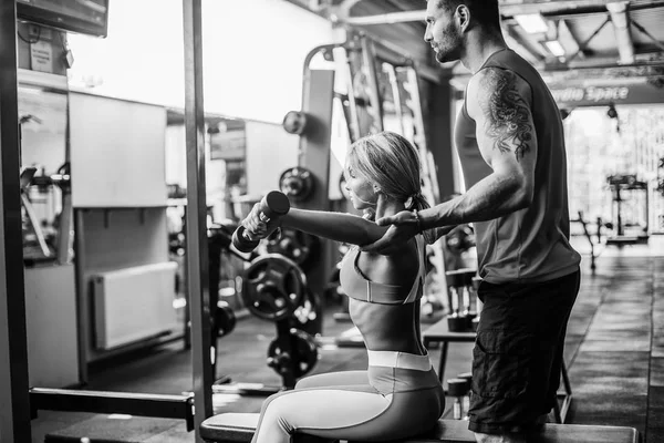 Chica deportiva haciendo ejercicios de peso con la ayuda de su entrenador personal en el gimnasio . — Foto de Stock