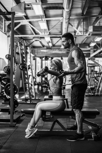 Sporty girl doing weight exercises with assistance of her personal trainer at gym. — Stock Photo, Image