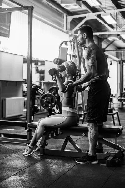 Ragazza sportiva che fa esercizi di peso con l'assistenza del suo personal trainer in palestra . — Foto Stock