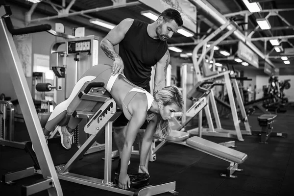 Sporty girl doing weight exercises with assistance of her personal trainer at gym. — Stock Photo, Image