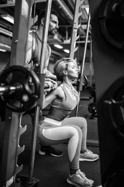 运动女孩做深蹲练习与她的私人教练在健身房的援助. — 图库照片