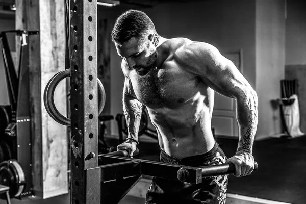 Hombre musculoso fuerte haciendo flexiones en barras irregulares en el gimnasio crossfit — Foto de Stock