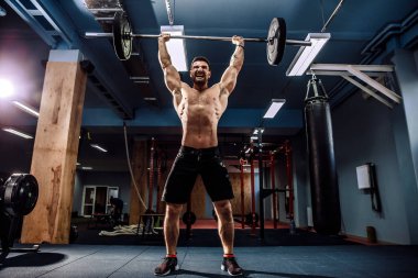 Modern fitness merkezinde kaslı bir fitness adamı halterle kafasına halteri indiriyor. Fonksiyonel eğitim.