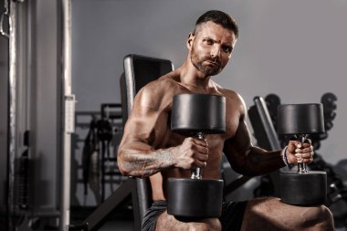 Yakışıklı ve kaslı bir adam, spor salonunda kameraya poz veriyor.