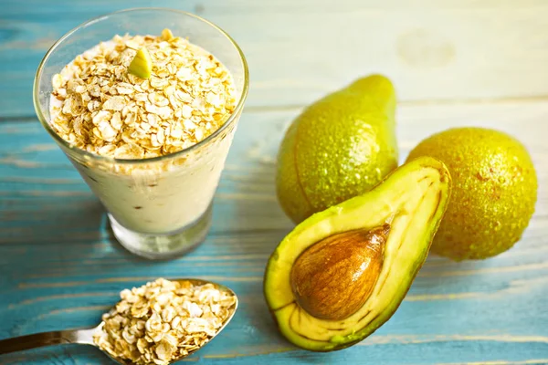 Sağlıklı gıda. Diyet Kahvaltı veya aperatif. Yoğurt, avokado, yulaf ezmesi gelen yeşil smoothies. Mavi ahşap masa üzerinde malzemelerle.
