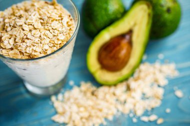 Sağlıklı gıda. Diyet Kahvaltı veya aperatif. Yoğurt, avokado, yulaf ezmesi gelen yeşil smoothies. Mavi ahşap masa üzerinde malzemelerle.