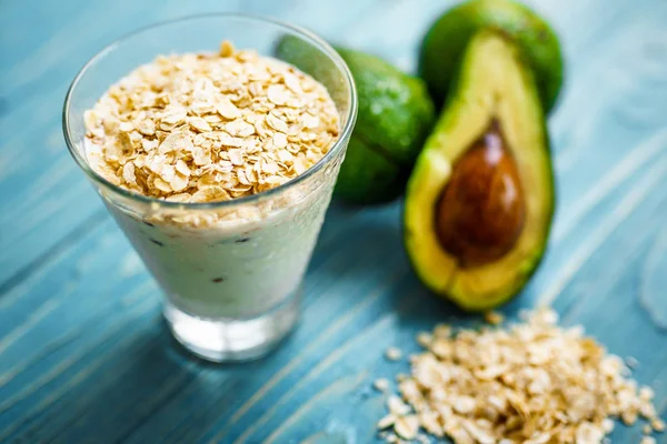 Sağlıklı gıda. Diyet Kahvaltı veya aperatif. Yoğurt, avokado, yulaf ezmesi gelen yeşil smoothies. Mavi ahşap masa üzerinde malzemelerle.