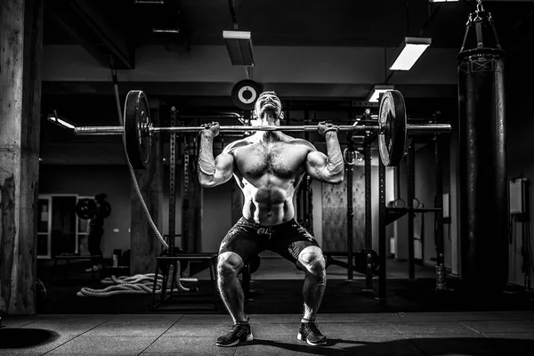 Een gespierde fitnessman die een halter over zijn hoofd tilt in een modern fitnesscentrum. Functionele opleiding. — Stockfoto