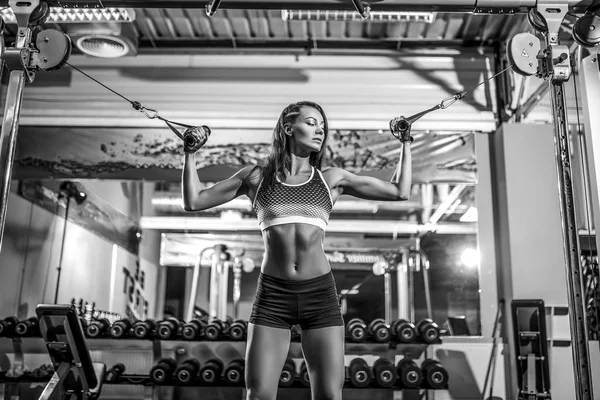 Woman flexing muscles on cable machine in gym — Stock Photo, Image