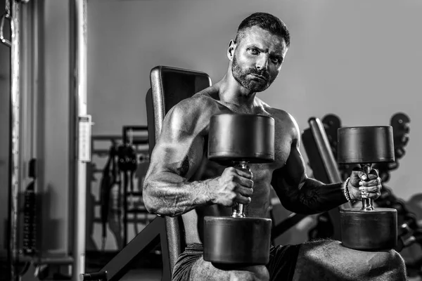 Yakışıklı ve kaslı bir adam, spor salonunda kameraya poz veriyor.