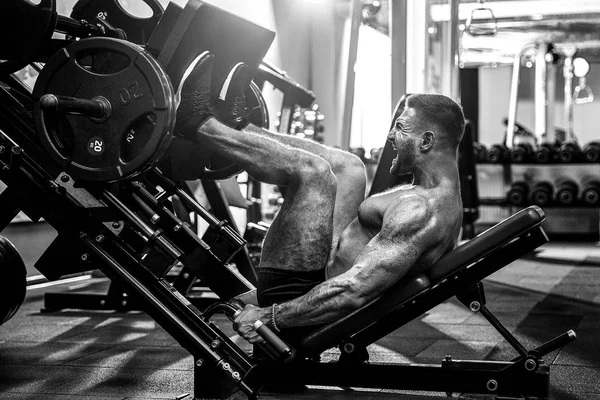Ο άνθρωπος χρησιμοποιώντας μια μηχανή τύπου στο γυμναστήριο. Ισχυρός άνδρας κάνει μια άσκηση στα πόδια της στον προσομοιωτή. — Φωτογραφία Αρχείου