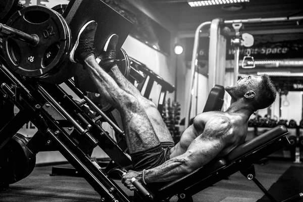 Hombre usando una máquina de prensa en un club de fitness. Hombre fuerte haciendo un ejercicio en sus pies en el simulador . — Foto de Stock