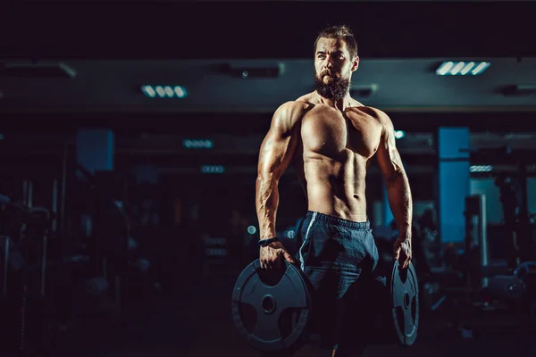 Atleta musculoso culturista hombre posando con pesas en el gimnasio . — Foto de Stock