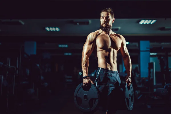 Spor salonunda dumbbells ile poz atlet kaslı vücut geliştirmeci adam. — Stok fotoğraf