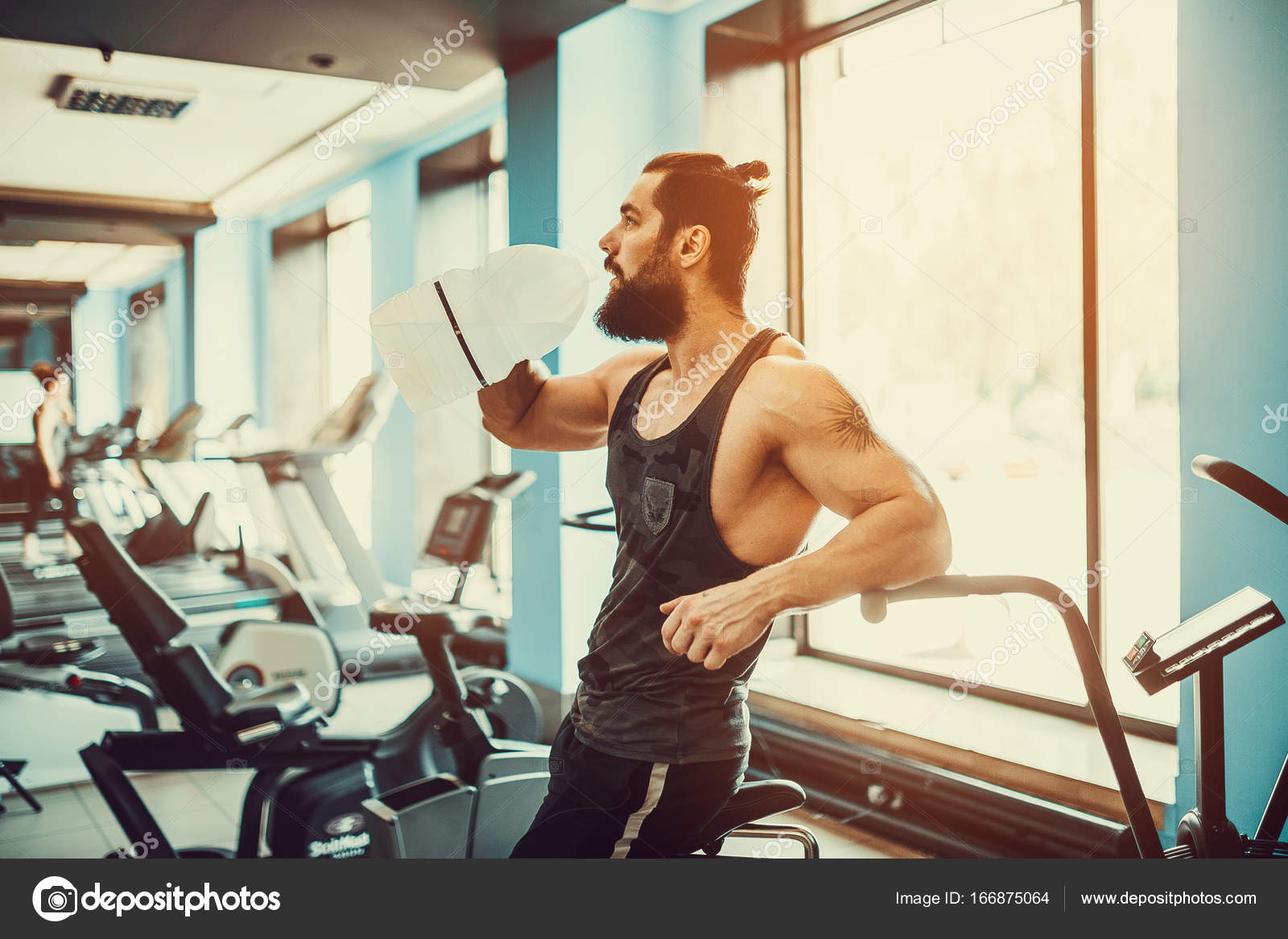 Guy relaxing after workout and hold or drink water from big bottle in
