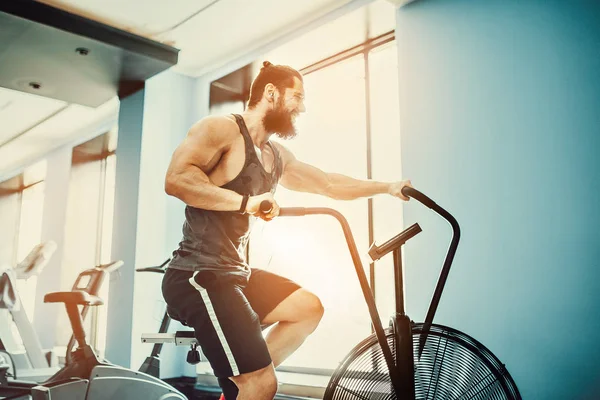 年轻人在健身房使用自行车运动。使用空气自行车锻炼运动量来找到健身房健身男. — 图库照片