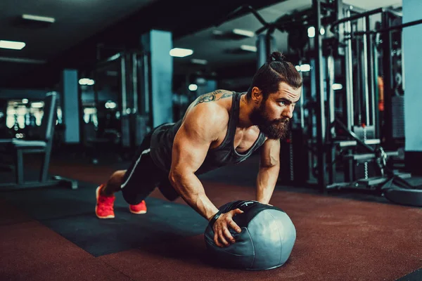 Hombre joven musculoso que usa ropa deportiva y hace posición de tablón mientras hace ejercicio en el suelo en el interior del loft —  Fotos de Stock