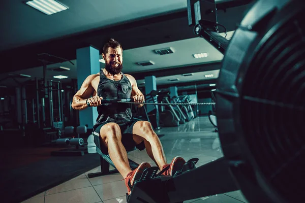 Gespierde fit man met roei-machine op sportschool — Stockfoto