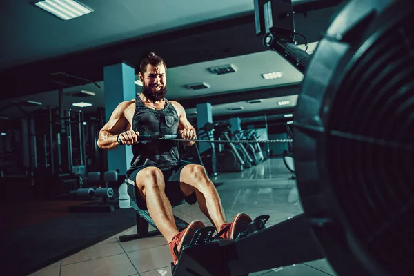 Muskulös vältränad man med roddmaskin på gym — Stockfoto