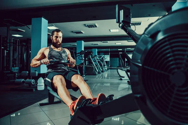 Muskularny mężczyzna dopasowania przy użyciu maszyny do wiosłowania w siłowni — Zdjęcie stockowe