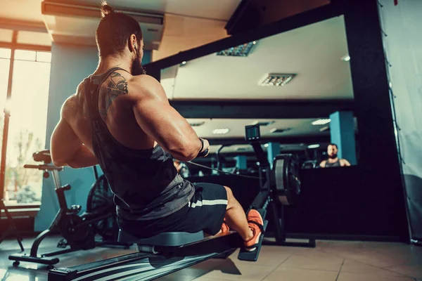 Muskulös vältränad man med roddmaskin på gym — Stockfoto