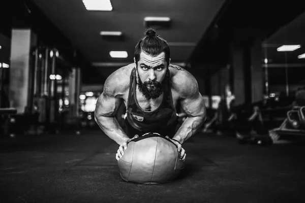 Hombre joven musculoso que usa ropa deportiva y hace posición de tablón mientras hace ejercicio en el suelo en el interior del loft — Foto de Stock