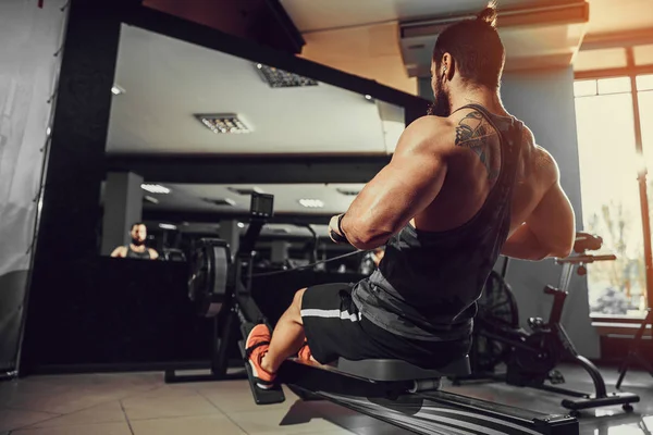 Muskulös vältränad man med roddmaskin på gym — Stockfoto