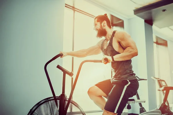 young man using exercise bike at the gym. Fitness male using air bike for cardio workout at crossfit gym.