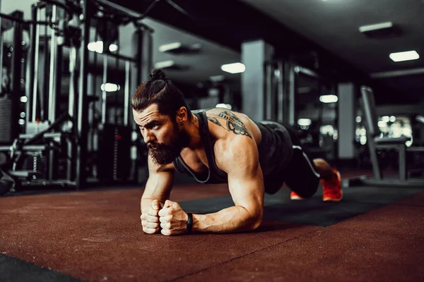 Çatı katı iç yerdeki egzersiz yaparken spor giyim ve iş tahta pozisyonu giyen kaslı genç adam — Stok fotoğraf