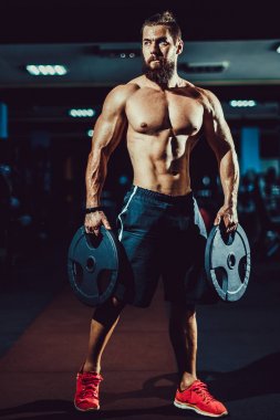 Spor salonunda dumbbells ile poz atlet kaslı vücut geliştirmeci adam.