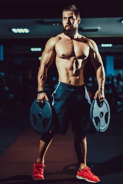 Spor salonunda dumbbells ile poz atlet kaslı vücut geliştirmeci adam. — Stok fotoğraf