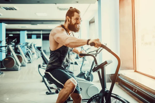 Jovem usando bicicleta de exercício no ginásio. Fitness masculino usando bicicleta de ar para treino cardio no ginásio crossfit . — Fotografia de Stock