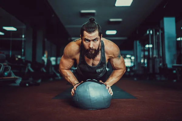 Hombre joven musculoso que usa ropa deportiva y hace posición de tablón mientras hace ejercicio en el suelo en el interior del loft —  Fotos de Stock