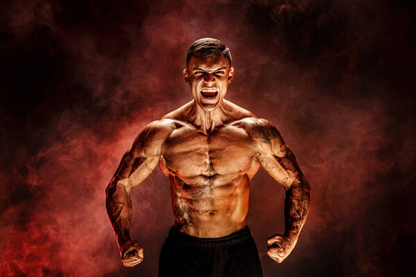 Bodybuilder posing. Fitness tattooed muscled man on red smoke background.