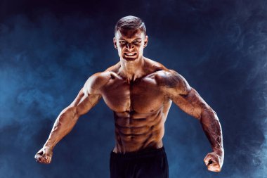 Vücut geliştirici pozu. Fitness karanlık arka planda kaslı bir adam. Motivasyon için kükreme.
