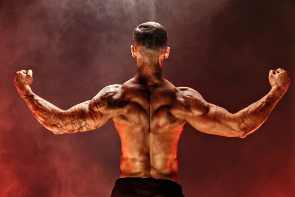 Vista posteriore dell'uomo irriconoscibile, muscoli forti che posano con le braccia abbassate nel fumo . — Foto Stock