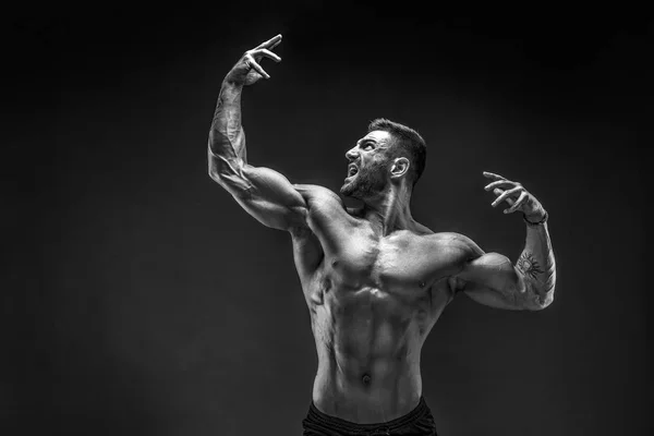 Bodybuilder θέτει. Γυμναστήριο μυώδης άνθρωπος σε σκούρο φόντο. — Φωτογραφία Αρχείου