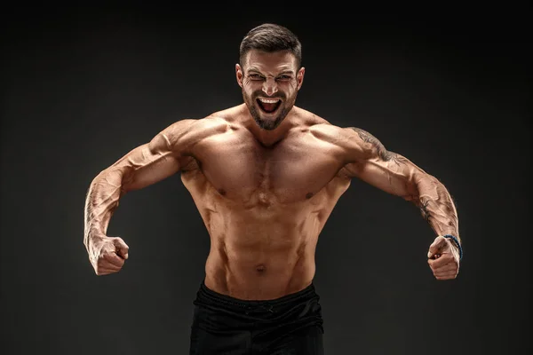 Culturista posando. Hombre musculoso fitness sobre fondo oscuro. Rugiendo por la motivación. — Foto de Stock