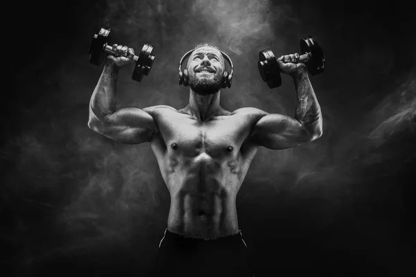 Músculos de entrenamiento de hombre con mancuernas en estudio sobre fondo oscuro — Foto de Stock