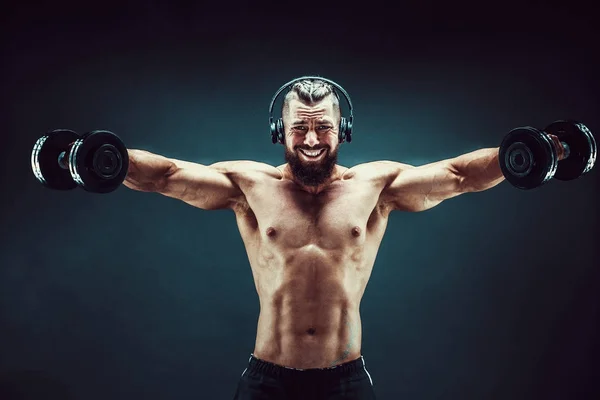 暗い背景上のスタジオにダンベルで男トレーニング筋肉. — ストック写真