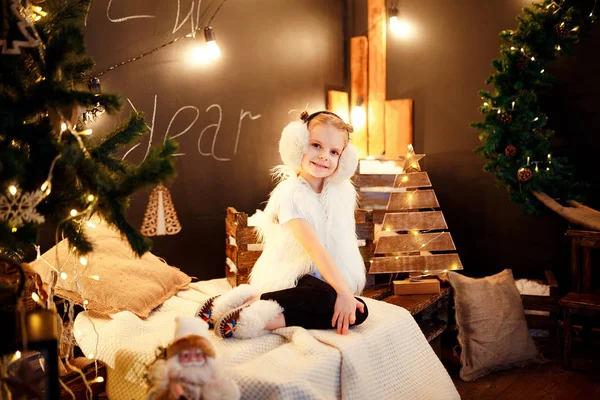Carino bambina in pelliccia paraorecchie seduto vicino all'albero di Natale — Foto Stock