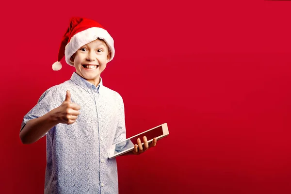 Joven santa boy haciendo el ok pulgares hacia arriba gesto mientras sostiene un —  Fotos de Stock