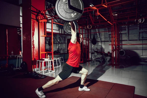 Muskelkräftiger Fitnessmann beim Kreuzheben einer Langhantel über dem Kopf in einem modernen Fitnesscenter. Functional Training. — Stockfoto