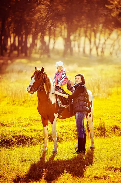 Маленька дівчинка їде на коні з матір'ю, що йде поруч — стокове фото