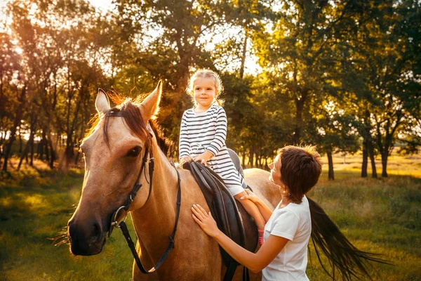 Маленькая девочка едет верхом на лошади со своей матерью, стоящей рядом — стоковое фото